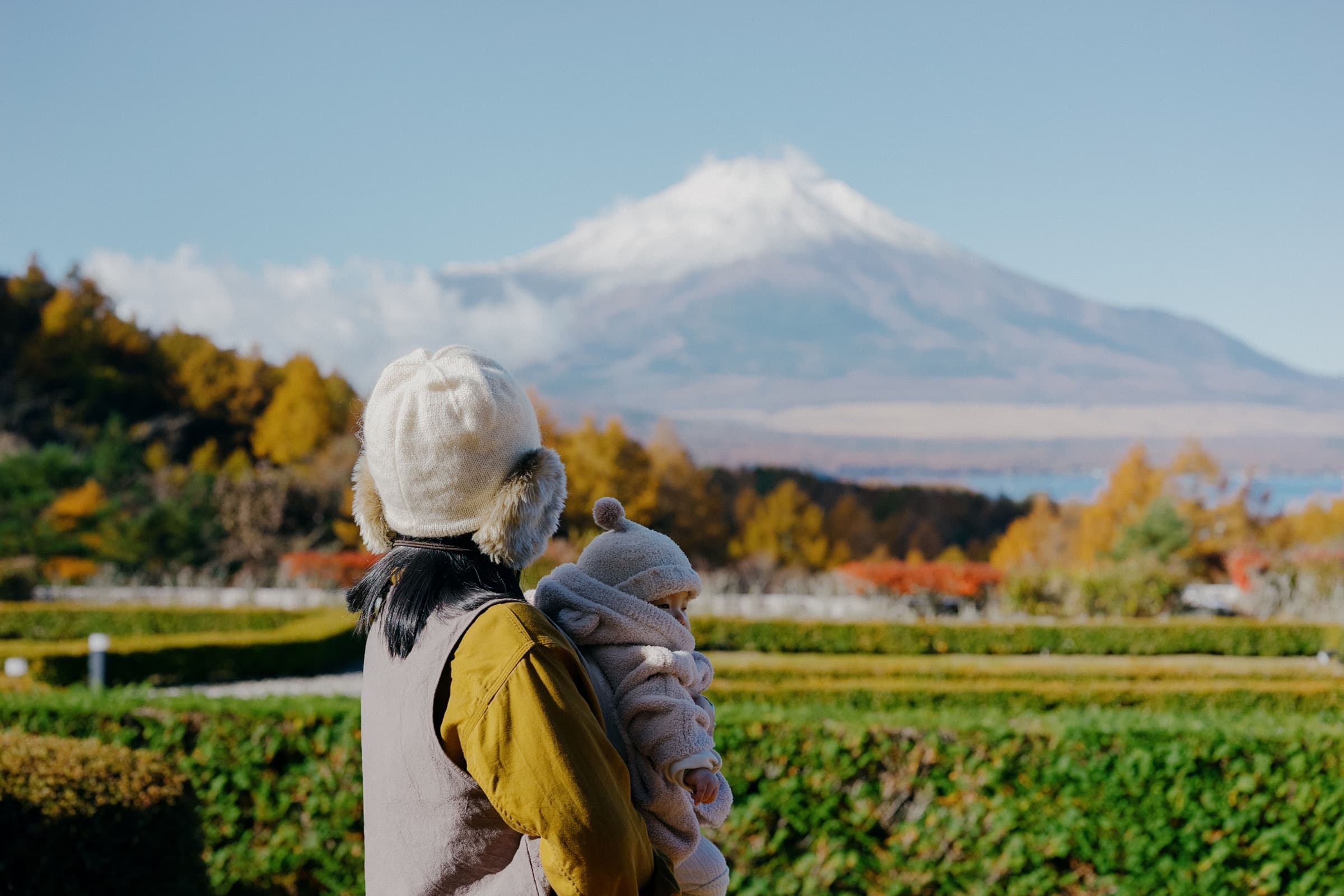 A parent holding a baby outdoors with Mount Fuji in the background