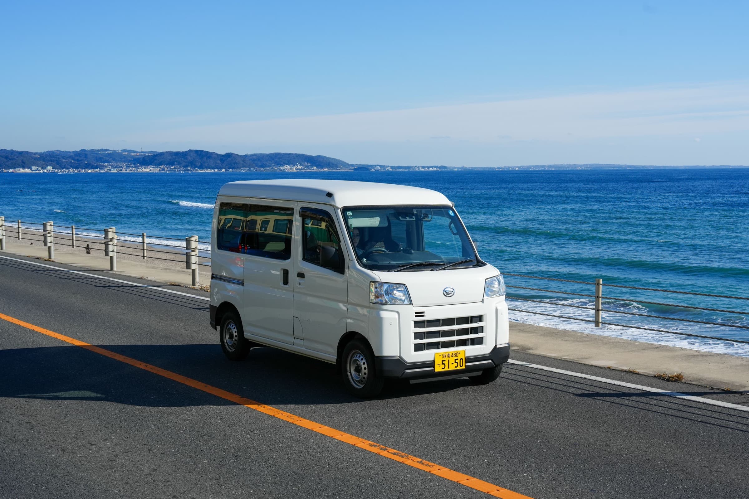 A small Japanese rental car driving beside a bright blue coastline