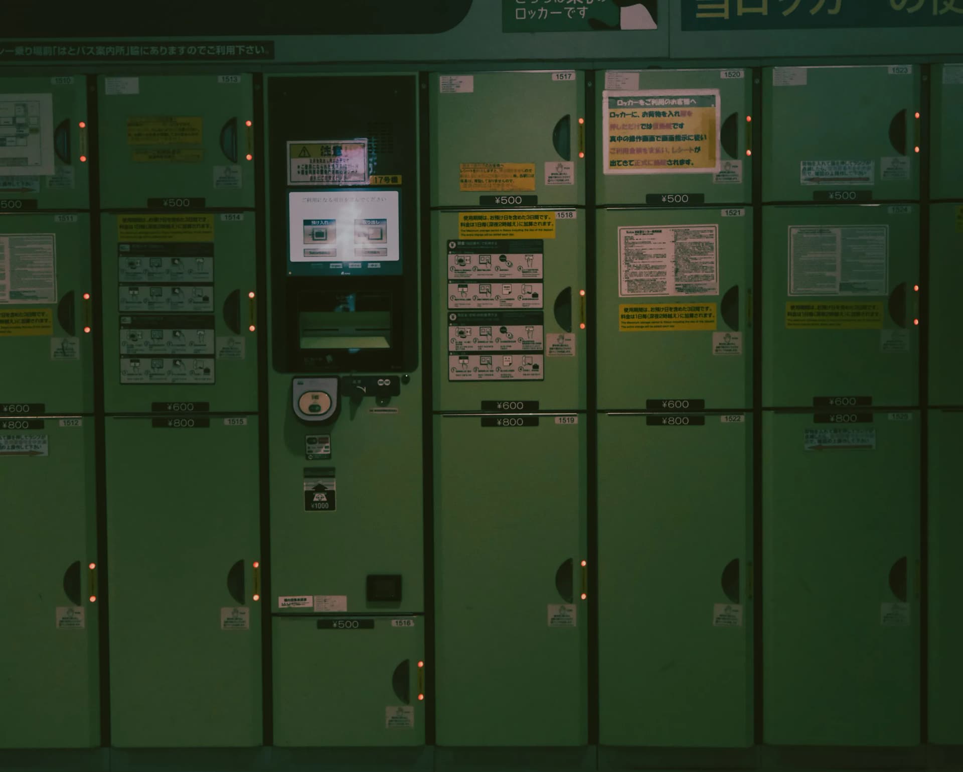 A bank of green luggage lockers in a Japanese station with a central payment screen