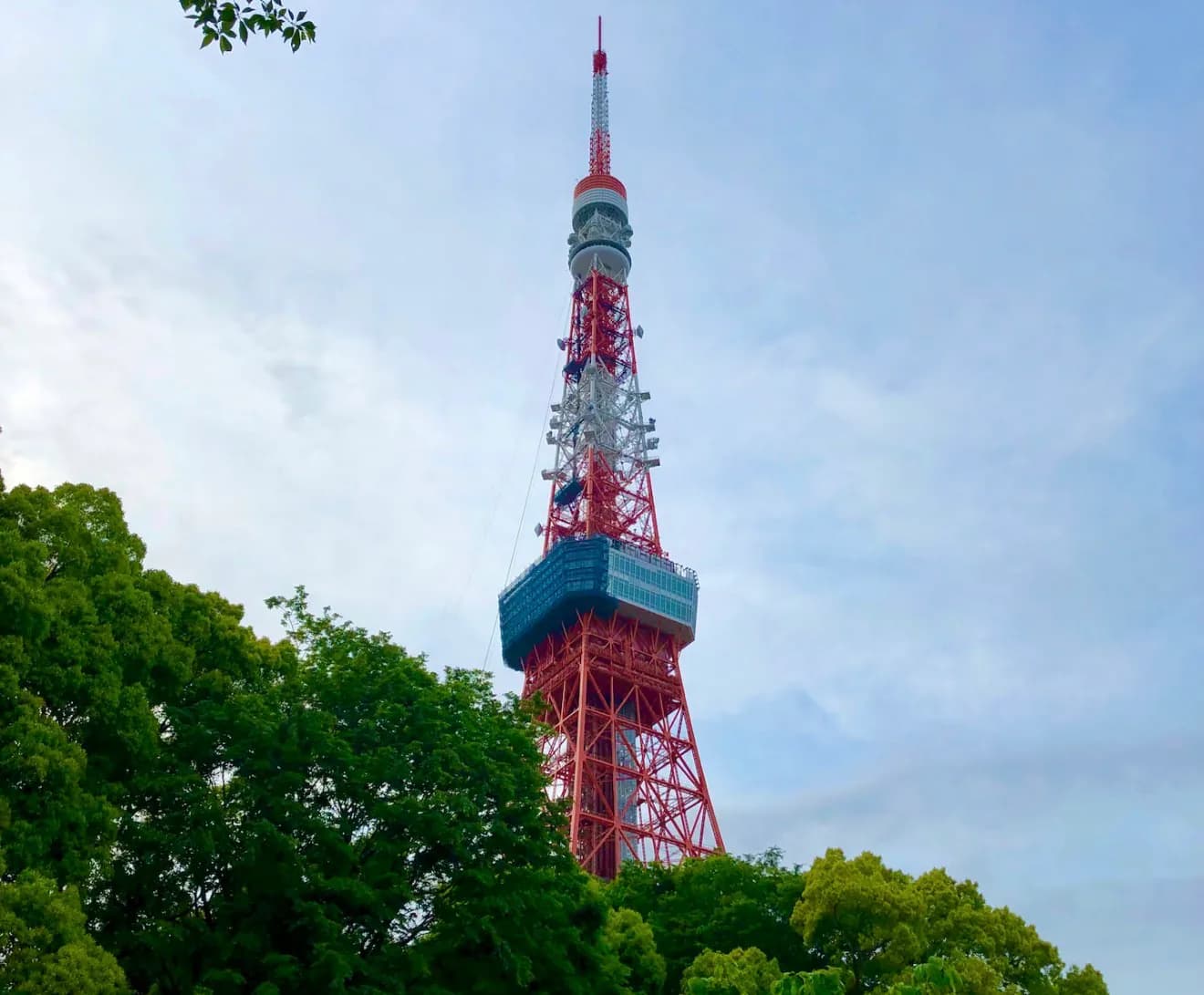 Tokyo Tower's red-and-white steel structure rising above green trees beneath a cloudy sky