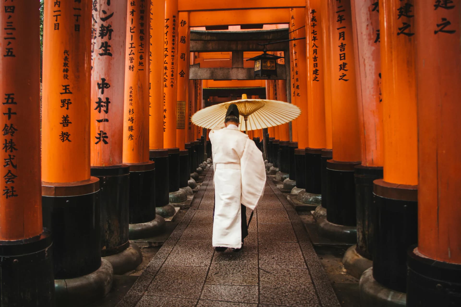 A person carrying a paper umbrella beneath the vermilion torii gates at Fushimi Inari in Kyoto