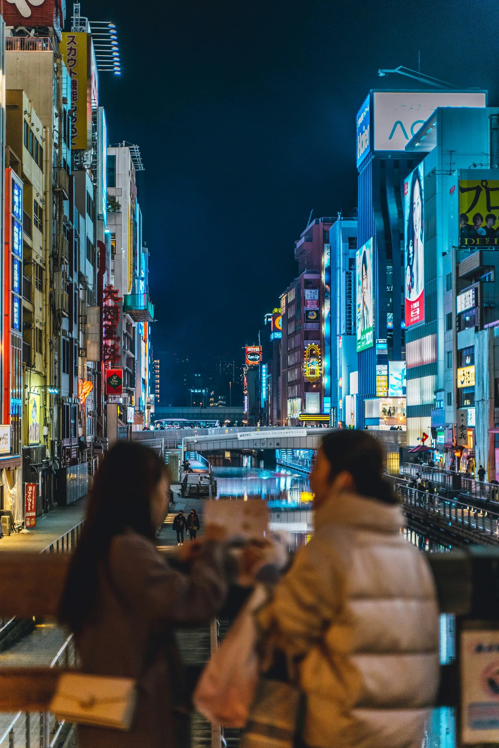 Visitors overlooking Dotonbori's illuminated canal at night in Osaka