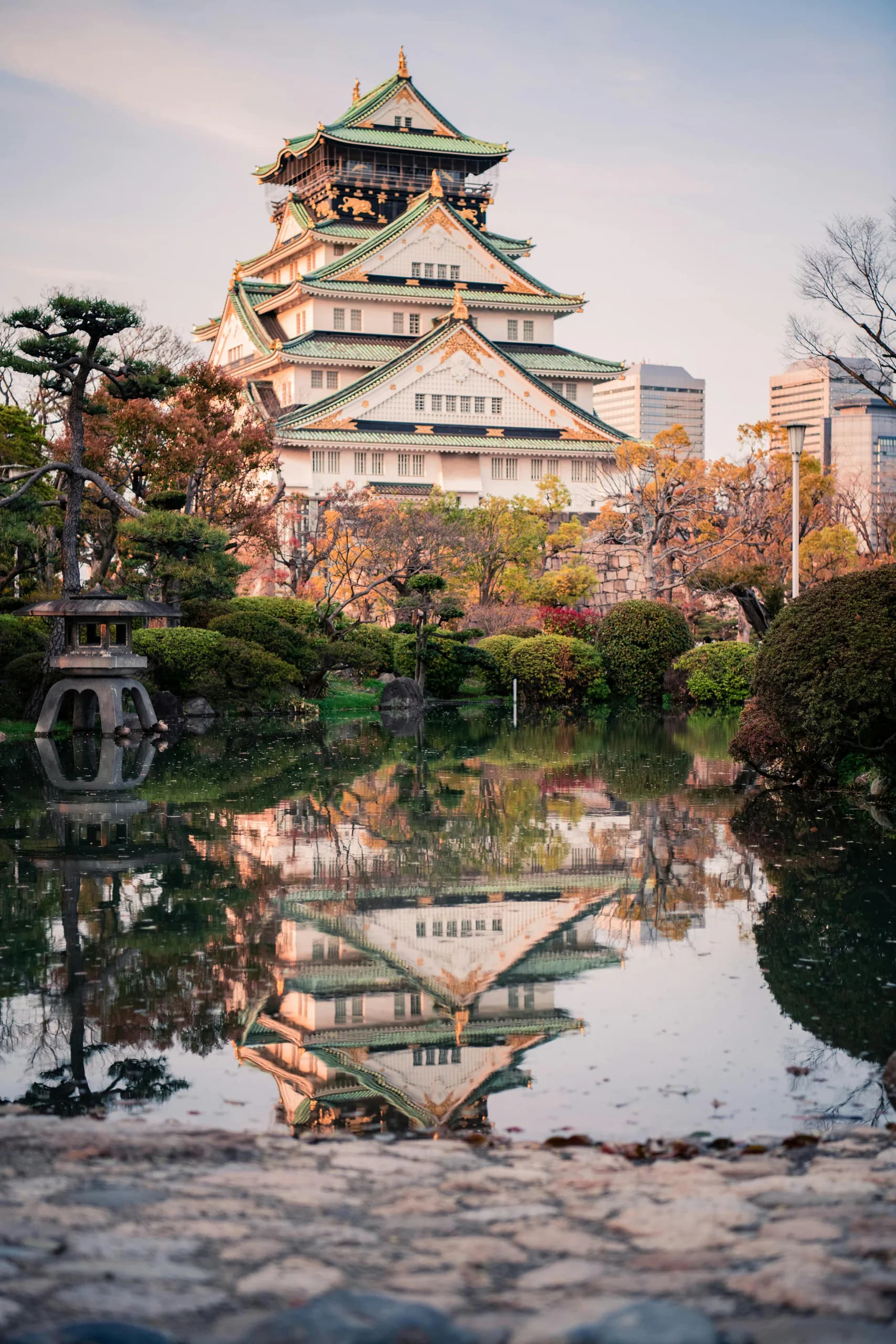 Osaka Castle reflected in a pond beneath autumn-colored trees